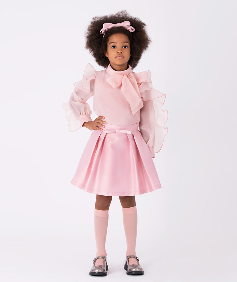 A statement outfit featuring a voluminous bow blouse with dramatic ruffle sleeves and a classic pleated skirt