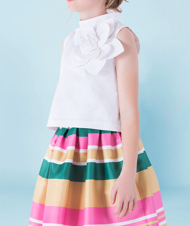 Classic white blouse with an oversized floral applique, styled with a colorful striped midi skirt in shades of pink, green, and gold