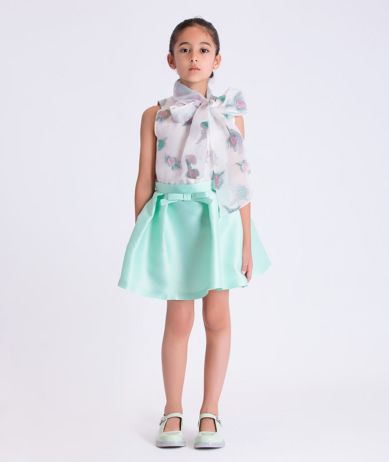 Young girl wearing a floral blouse and light blue skirt on a white background