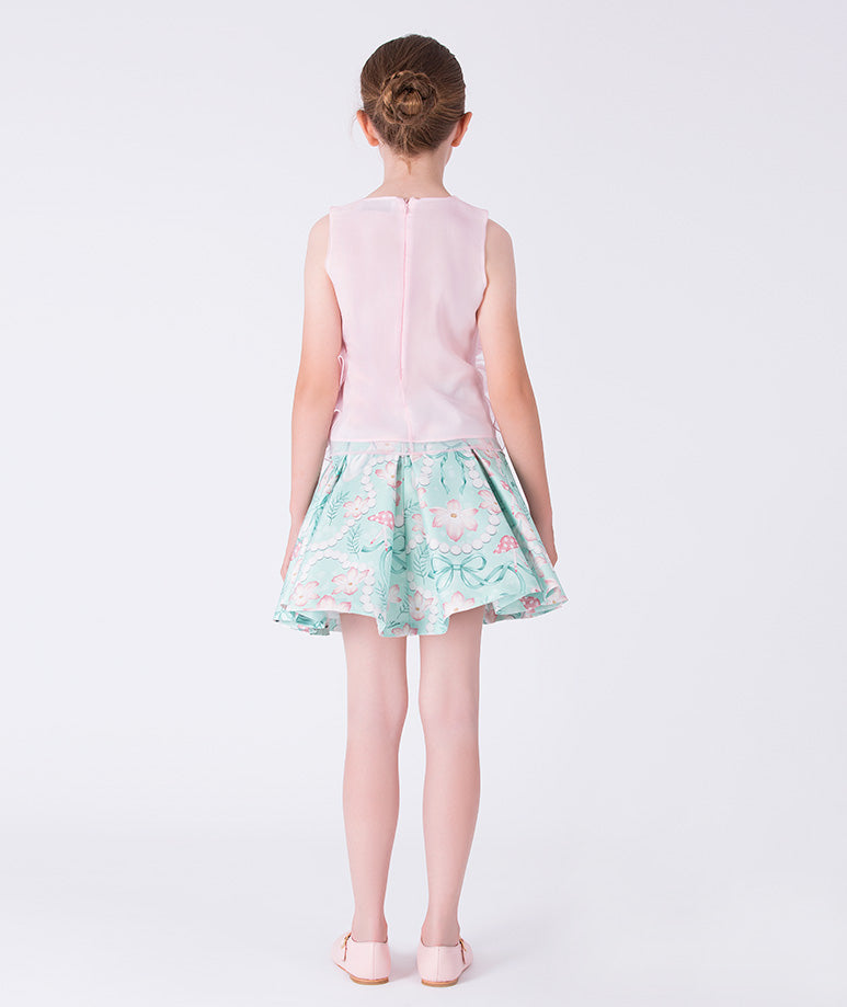 Young girl wearing a light pink top and floral skirt on a white background