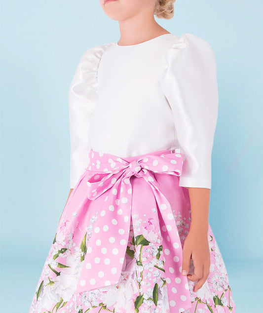 satin balloon sleeve white blouse with pink floral skirt that has a big polka dotted bow on the waist