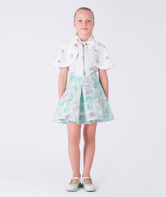 7 years old girl wearing a white blouse with a bow and a floral skirt on a white background