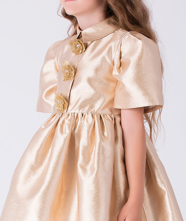 Close-up of metallic gold girls dress featuring decorative floral brooch appliqués and classic pointed collar detail.