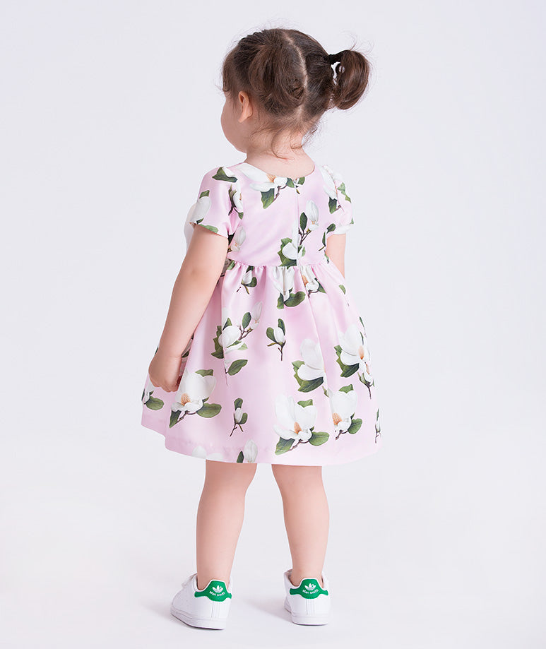 Baby girl wearing a pink floral dress with flower appliqué detail by Mama Luma