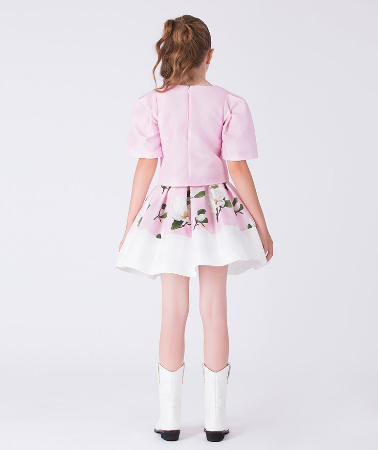 Back view of a pink floral girls occasion outfit featuring a short sleeve structured top and a matching flared skirt with contrast hem, styled for birthdays, weddings, garden parties, and special occasions, available in sizes 3–12