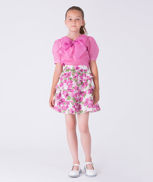 Sheer puff sleeve girls outfit worn by a 6-year-old girl, featuring a statement bow top and tiered floral skirt for special occasions.