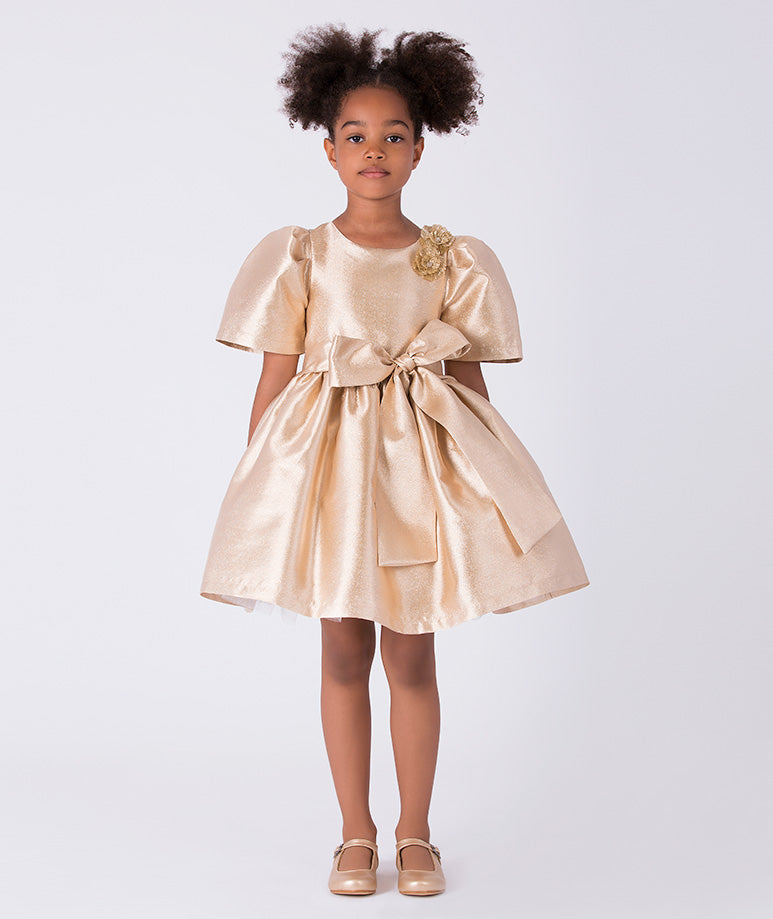 Front view of gold metallic girls dress with puff sleeves, floral shoulder embellishment and statement waist bow.