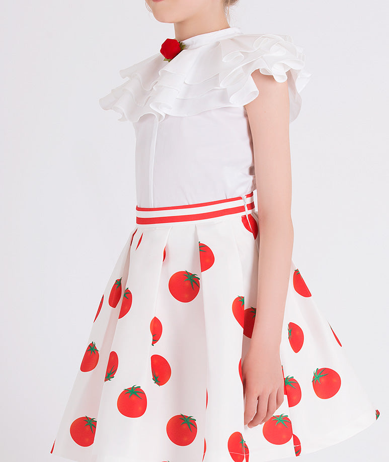 ecru ruffled blouse with a red rose brooch and an ecru skirt with tomato prints